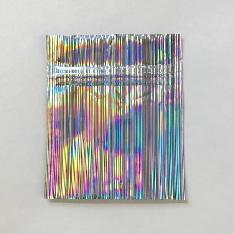 May include: A silver iridescent resealable pouch with a zipper closure. The pouch is made of a thin, flexible material and has a holographic finish.
