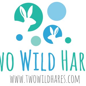 Może przedstawiać: Logo firmy o nazwie "Two Wild Hares" z tekstem "www.twowildhares.com" poniżej. Logo przedstawia dwa białe kr&oacute;liki w niebieskich i zielonych okręgach, z dodatkowymi niebieskimi i zielonymi okręgami rozrzuconymi wok&oacute;ł.