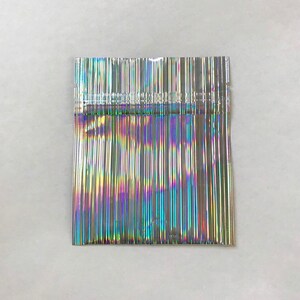 May include: A silver iridescent plastic bag with a heat-sealed opening. The bag is made of thin, flexible plastic and has a holographic finish.