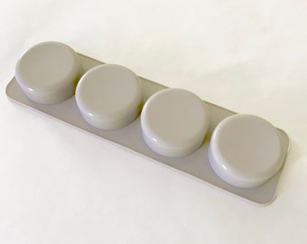 Puede incluir: Un molde de silicona gris con cuatro cavidades redondas para hacer jabón u otras manualidades.