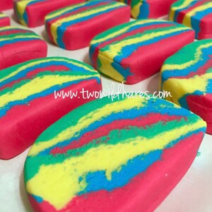 Puede incluir: Primer plano de barras de jab&oacute;n coloridas y en espiral. El jab&oacute;n es rojo, amarillo, azul y verde. El jab&oacute;n tiene forma de rect&aacute;ngulo y una superficie lisa y brillante. El jab&oacute;n est&aacute; dispuesto en una fila sobre una superficie blanca. El texto "www.twowildhares.com" es visible en la imagen.