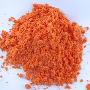 May include: A close-up of a pile of orange bath salts. The salts are fine and granular, and they have a bright orange color.