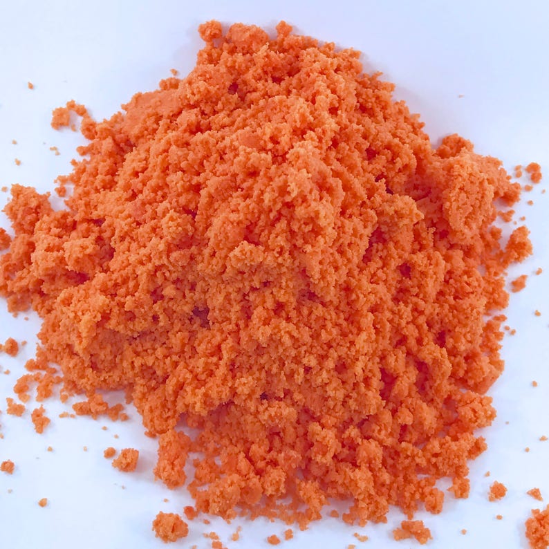 May include: A close-up of a pile of orange bath salts. The salts are fine and granular, and they have a bright orange color.