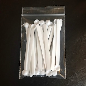 May include: A clear plastic bag filled with white plastic measuring spoons. The spoons have a rounded end and a long, thin handle.