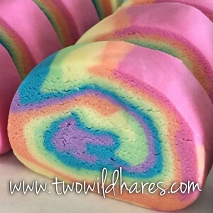 Puede incluir: Primer plano de una galleta de espiral arco&iacute;ris. La galleta es rosa, naranja, amarilla, verde, azul y morada. La galleta est&aacute; enrollada en forma de tronco y tiene un patr&oacute;n de espiral. La galleta est&aacute; sobre una superficie blanca. www.twowildhares.com