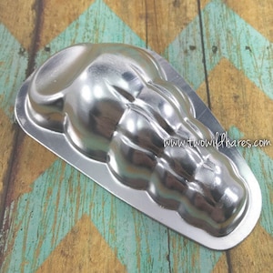 May include: A silver metal mold shaped like a seashell. The mold has a smooth, shiny surface and is designed for making chocolate or other treats.