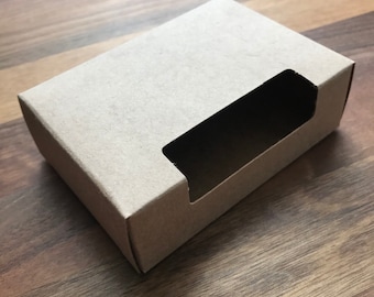 May include: A brown cardboard box with a rectangular window cut out of the top. The box is designed for packaging small items.