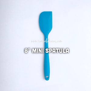 Peut inclure: Une mini spatule de 8 pouces en silicone de couleur bleu vif. La spatule a une tête arrondie et un long manche.