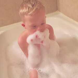 Puede incluir: Un ni&ntilde;o peque&ntilde;o est&aacute; sentado en una ba&ntilde;era llena de burbujas. El ni&ntilde;o est&aacute; sosteniendo un pu&ntilde;ado de burbujas frente a su cara.