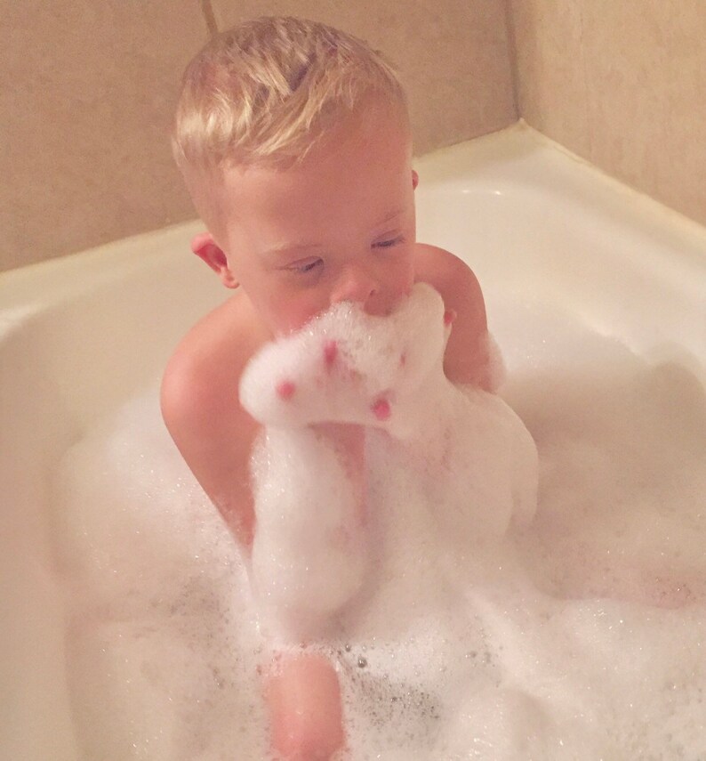 Puede incluir: Un ni&ntilde;o peque&ntilde;o est&aacute; sentado en una ba&ntilde;era llena de burbujas. El ni&ntilde;o est&aacute; sosteniendo un pu&ntilde;ado de burbujas frente a su cara.