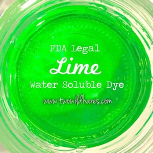 May include: A close-up of a jar of green water-soluble dye. The label reads "FDA Legal Lime Water Soluble Dye" and "www.twowildhares.com".