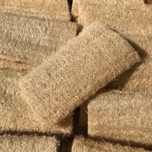 May include: A collection of beige loofah sponges, rectangular in shape, with a natural, fibrous texture. One sponge is positioned on top of the others, highlighting its form. These eco-friendly bath accessories are made from dried gourds.