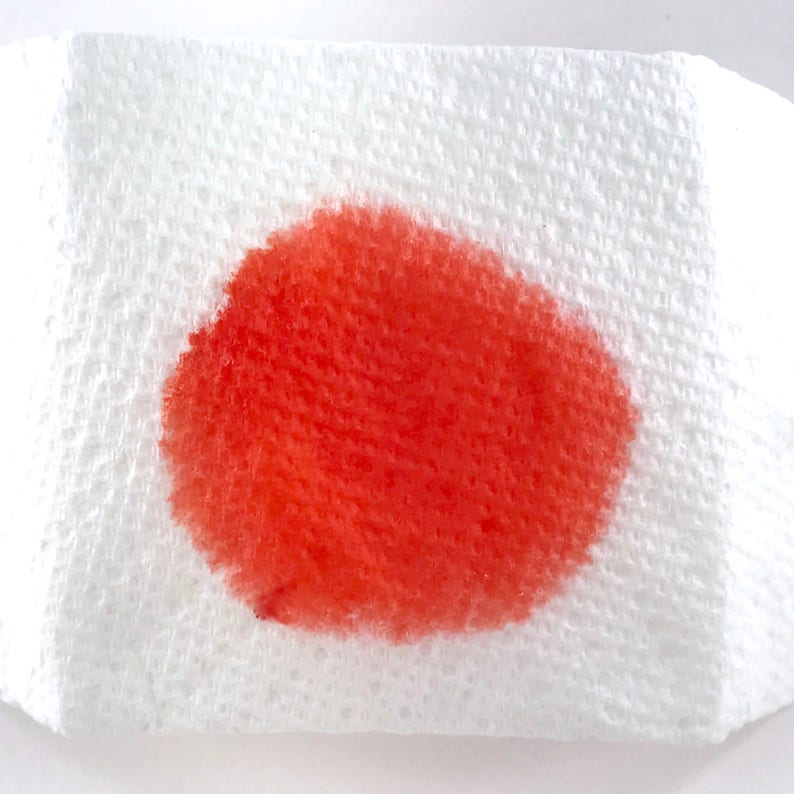 May include: A close-up of a white paper towel with a bright red stain in the center.