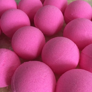 May include: A group of pink bath bombs arranged in a pile. The bath bombs are round and have a smooth, textured surface.