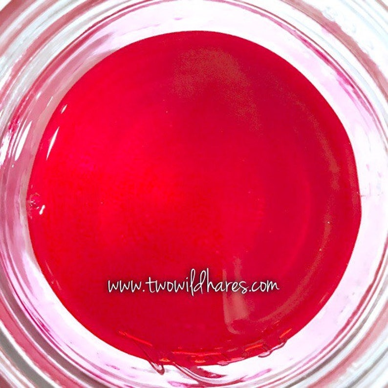 May include: A close-up of a glass jar filled with a bright red liquid. The liquid is clear and has a slight sheen. The jar is sitting on a white surface. The text "www.twowildhares.com" is visible at the bottom of the jar.