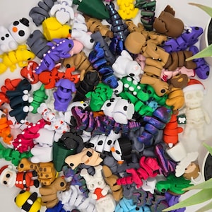 May include: A large collection of colorful, 3D printed figurines. The figurines are made in a variety of shapes and sizes, including animals, people, and abstract designs. The figurines are all made in a bright, vibrant color palette.