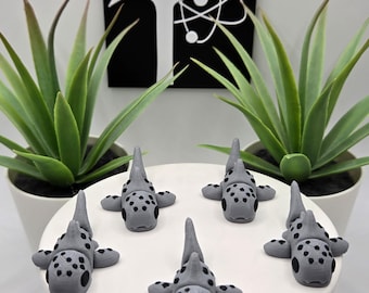 May include: Five small gray and black shark figurines with black eyes and spots. The sharks are arranged in a circle on a white surface.