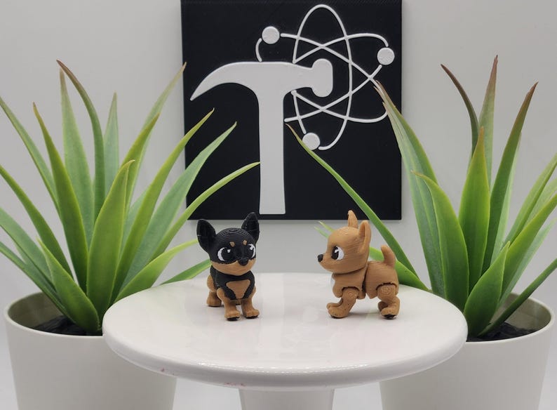May include: Two small, detailed chihuahua figurines, one black and tan, the other tan, stand on a white pedestal. The background features a black square with a white atom symbol and a hammer. Green plants in white pots flank the pedestal.