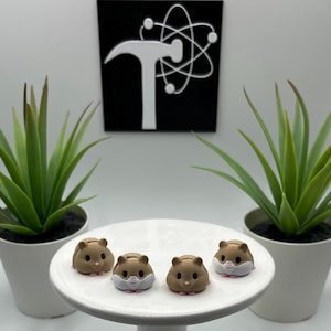 May include: Four small, brown hamster figurines with pink feet and white faces are arranged on a white, round pedestal. Two potted green plants flank the pedestal. A black and white graphic is in the background.
