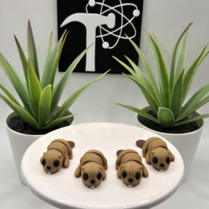 May include: Four brown beaver figurines on a white plate. The beavers are facing the camera and have black eyes. The plate is on a white surface.