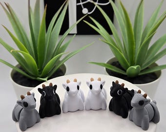 May include: Six small, 3D printed goat figurines in various colors, including black, white, and gray. The goats are sitting on a white plate.