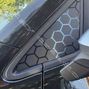 Peut inclure: Détail d'une voiture noire avec un motif en nid d'abeille sur la vitre triangulaire. Le motif géométrique est visible, avec le rétroviseur latéral en vue. La peinture de la voiture est brillante.