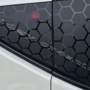 May include: Black car window featuring a honeycomb design. The window is tinted, with the pattern contrasting against the dark glass. The text "Cidgy Création" is displayed on the window.