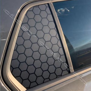 Könnte beinhalten: Ein Autofenster mit einem geometrischen Wabenmuster auf dem Glas. Das Muster ist dunkelgrau, und das Fenster wird von einem hellgrauen Rahmen umgeben. Das Fenster ist teilweise geöffnet.