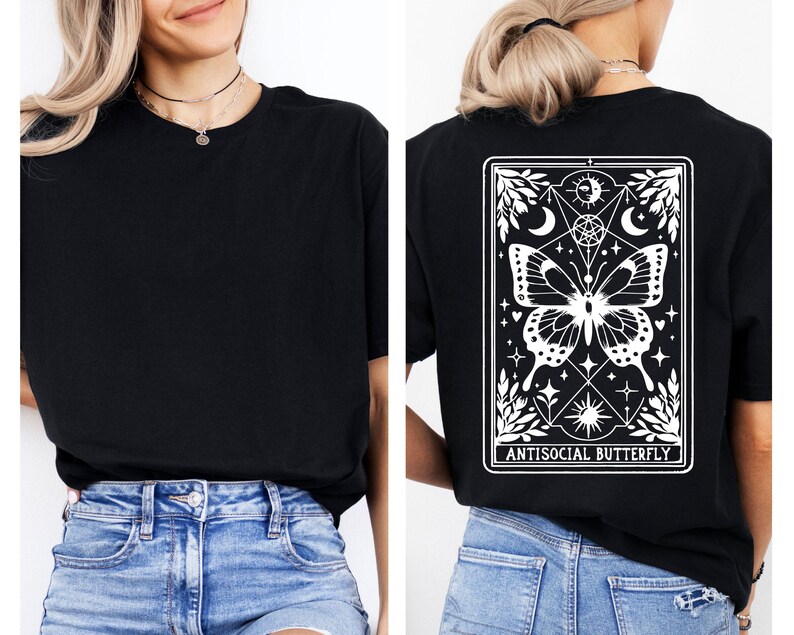 a woman wearing a black t-shirt with a graphic design on the back. The design features a butterfly and various celestial elements, including a moon and stars. The woman is also wearing blue jeans and a necklace.