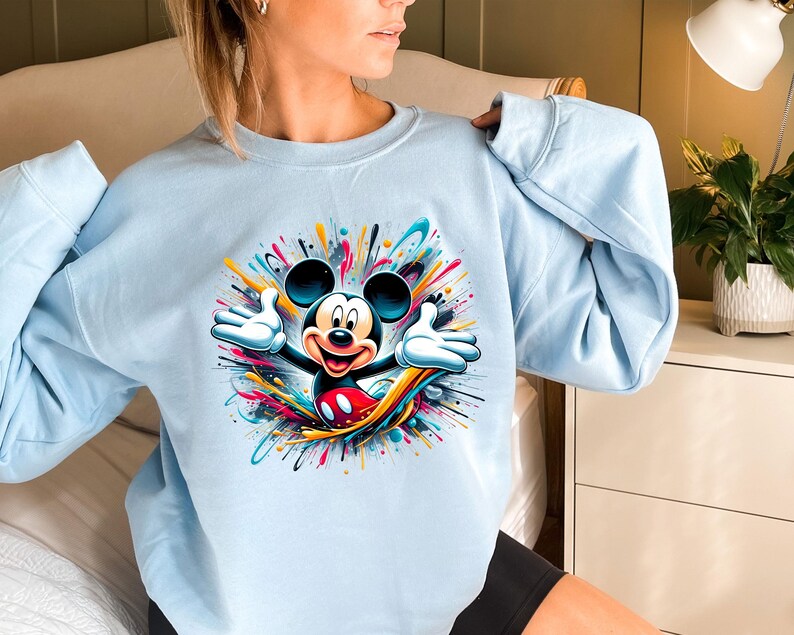 a woman sitting on a bed wearing a mickey mouse sweatshirt