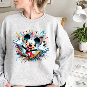 a woman sitting on a bed wearing a mickey mouse sweatshirt