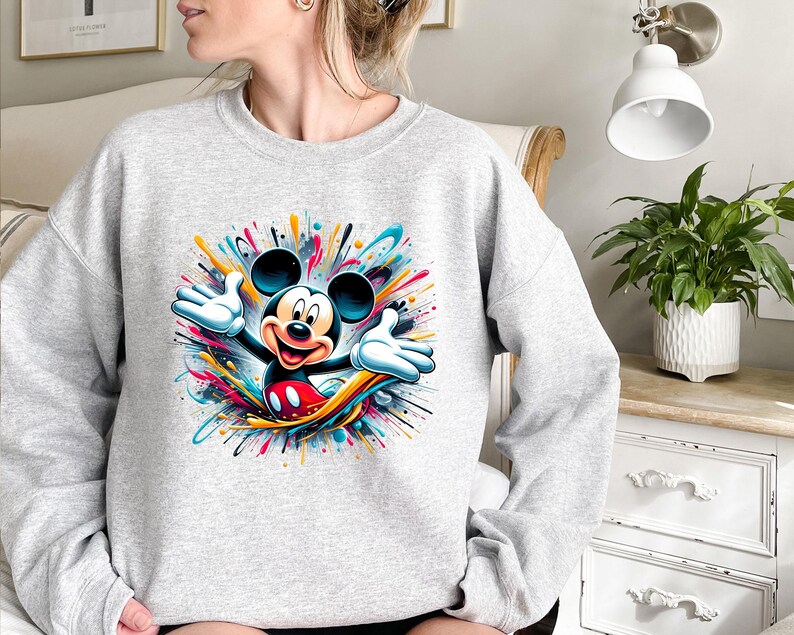 a woman sitting on a bed wearing a mickey mouse sweatshirt