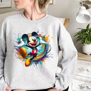 a woman sitting on a bed wearing a mickey mouse sweatshirt