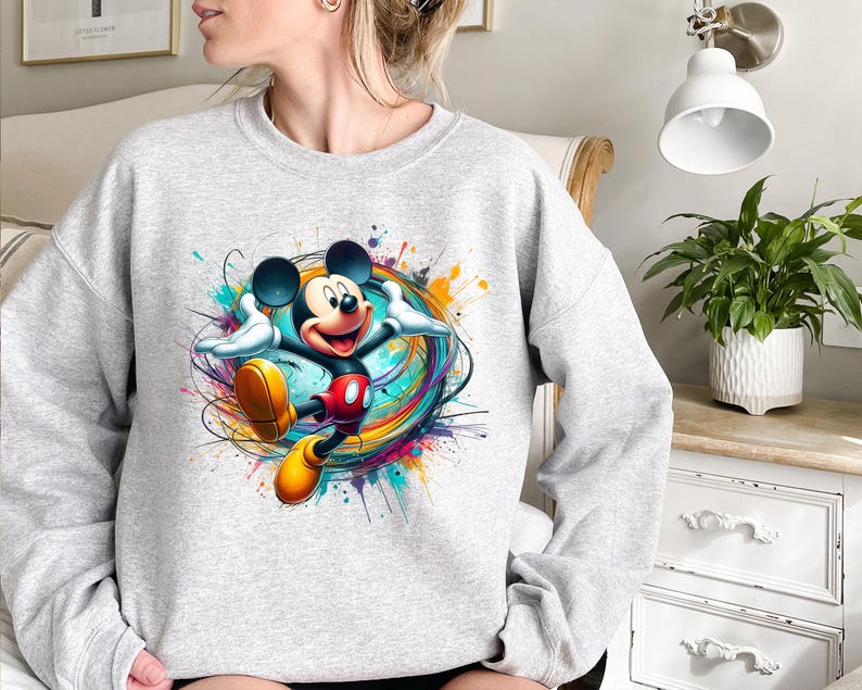 a woman sitting on a bed wearing a mickey mouse sweatshirt