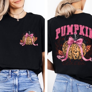 Pode incluir: Camiseta preta com abóbora com estampa de leopardo, laço rosa e folhas de outono. As palavras "PUMPKIN" e "Season" em rosa estão nas costas da camiseta.