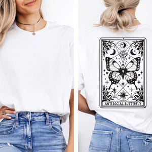 A woman wearing a white t-shirt with a graphic design on the back, featuring a butterfly and various symbols.