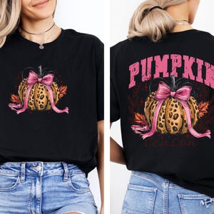 May include: Black t-shirt with a leopard print pumpkin design, a pink bow, and autumn leaves. The back of the shirt displays the text "PUMPKIN Season" in pink. A seasonal graphic tee.