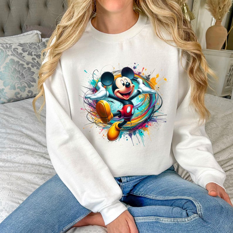 a woman sitting on a bed wearing a mickey mouse sweatshirt