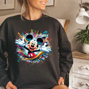 a woman sitting on a bed wearing a mickey mouse sweatshirt