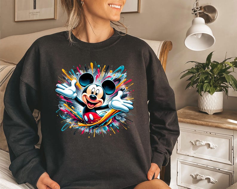 a woman sitting on a bed wearing a mickey mouse sweatshirt