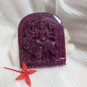 May include: A carved purple stone figurine of a Hindu deity riding a lion. The figurine is in a standing position and has a detailed design.