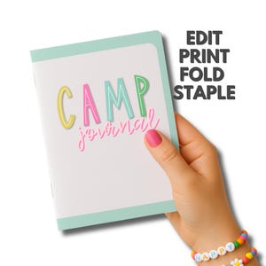 Peut inclure: Un journal blanc avec une bordure vert menthe et les mots "CAMP journal" en lettres color&eacute;es et ludiques. Le texte "EDIT PRINT FOLD STAPLE" est imprim&eacute; sur le c&ocirc;t&eacute; droit. Le journal est tenu par une main avec du vernis &agrave; ongles rose.