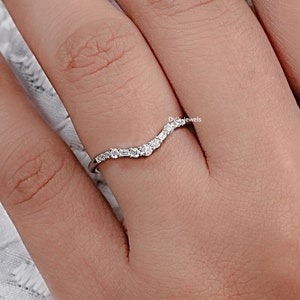 May include: A delicate silver ring with a curved, V-shaped band adorned with small, sparkling diamonds.