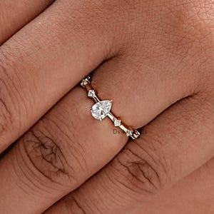 May include: A delicate gold ring with a pear-shaped diamond and smaller diamonds set along the band.