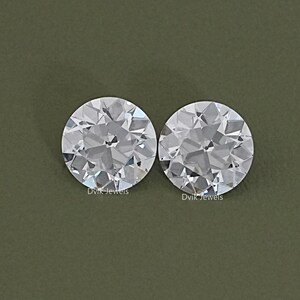 May include: Two clear round gemstones on a green background. The gemstones are faceted and have a slight sparkle.