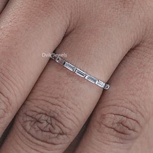 May include: A silver ring with a row of small, rectangular, clear stones. The ring is on a person's finger.