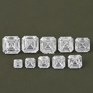 May include: Assortment of clear, square-shaped, faceted gemstones of varying sizes. The gemstones are arranged in a row from largest to smallest. The text "Dvik Jewels" is visible in the image.