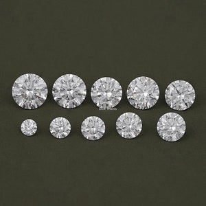 May include: A collection of ten round, clear, faceted gemstones. The gemstones are arranged in a row on a dark green background.