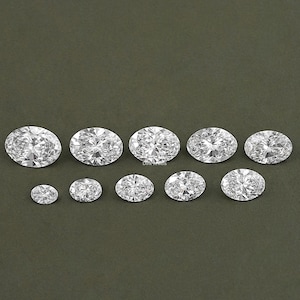 May include: A set of ten oval-shaped, clear, faceted gemstones. The gemstones are arranged in a row, with the largest gemstone in the center and the smallest gemstone on either end.