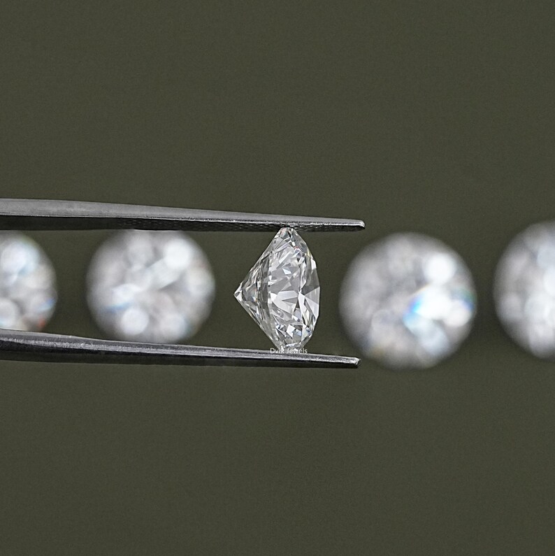 May include: A close-up of a diamond held in tweezers. The diamond is clear and sparkling. There are other diamonds out of focus in the background.
